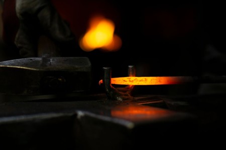 Artisan ferronnier forgeant une pièce métallique dans son atelier