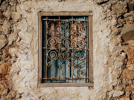 Fenêtre ancienne avec grille en fer forgé décorative sur une façade en pierre